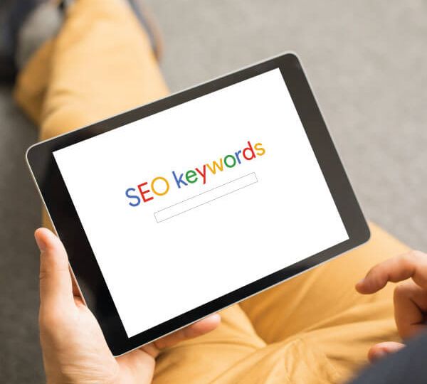Person holding a tablet displaying the words "SEO keywords" on the screen, symbolizing Skrivanek’s Google Ads and SEO translations, Meta Ads, and digital marketing services.