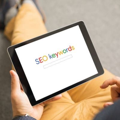 Person holding a tablet displaying the words "SEO keywords" on the screen, symbolizing Skrivanek’s Google Ads and SEO translations, Meta Ads, and digital marketing services.