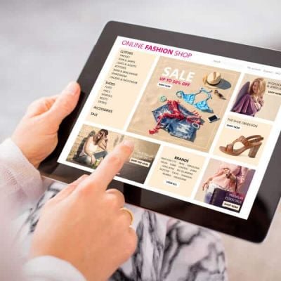 Person browsing a localized online fashion shop on a tablet, featuring global sale promotions, representing Skrivanek"s advanced localisation solutions.
