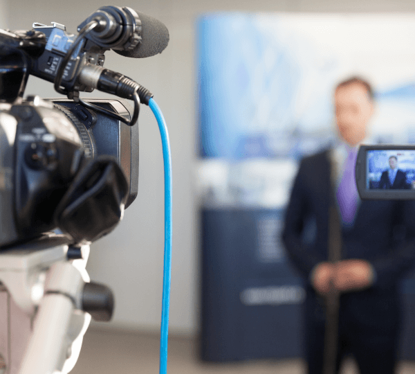 A professional video camera films the speaker, symbolising video material subtitling services.