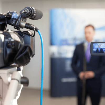 A professional video camera films the speaker, symbolising video material subtitling services.