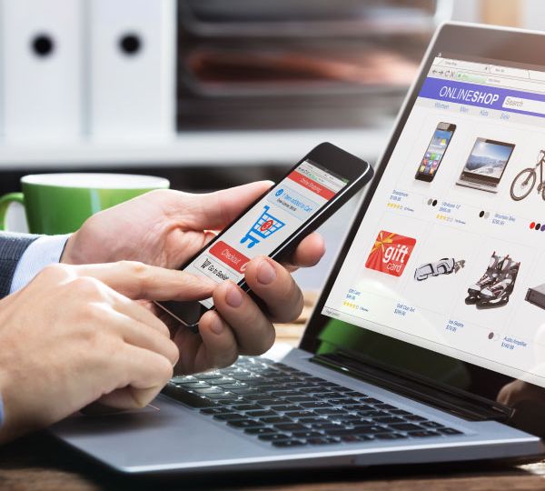 Person holding a smartphone and looking at an e-shop on a laptop, symbolising website metadata translation for digital content.