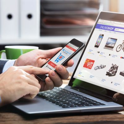 Person holding a smartphone and looking at an e-shop on a laptop, symbolising website metadata translation for digital content.