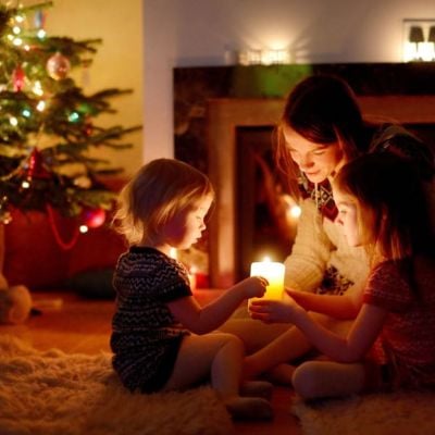 A family enjoying Christmas traditions by candlelight near a decorated tree and fireplace, reflecting the cultural diversity celebrated by Skrivanek Baltic.