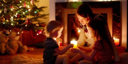 Unique Christmas traditions from 12 countries around the world | Skrivanek Baltic A family enjoying Christmas traditions by candlelight near a decorated tree and fireplace, reflecting the cultural diversity celebrated by Skrivanek Baltic.