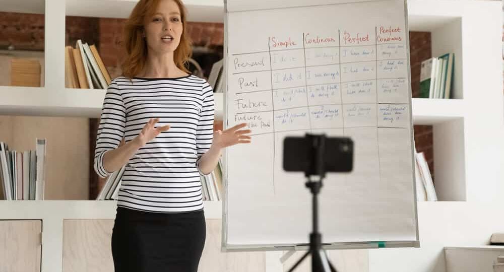 A woman presenting English grammar tenses on a flip chart while recording a training video—illustrating Skrivanek Baltic’s professional training video translation services.