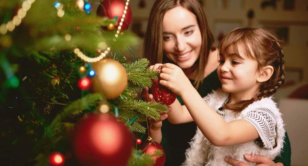 Mother and daughter decorating a Christmas tree with red and gold ornaments, symbolizing festive traditions and togetherness supported by Skrivanek Baltic’s multilingual services.