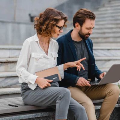 Divi profesionāļi strādā ar klēpjdatoru pilsētvidē, apspriežot digitālus risinājumus un interaktīvās platformas