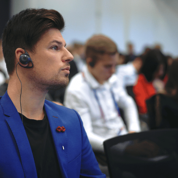 Konferences dalībnieks ar austiņām un uztveršanas ierīci, kas izmanto sinhronās tulkošanas aprīkojumu nelielai grupai.