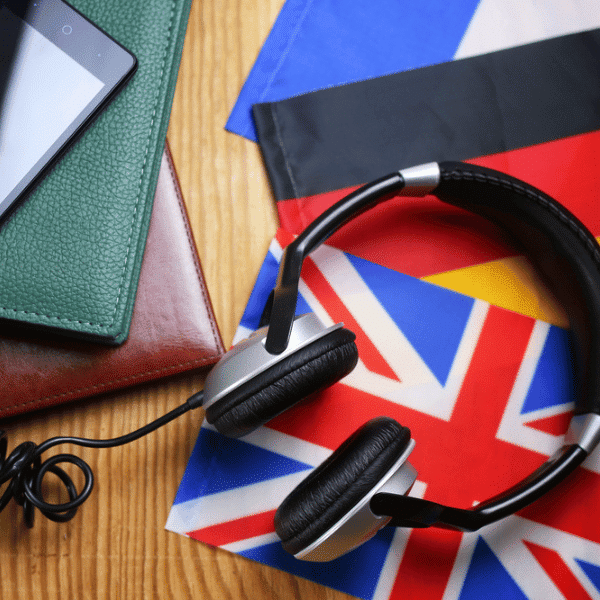 Galda virsma ar karogiem, austiņām, planšeti un piezīmju blokiem, attēlojot tūristu gidu aprīkojuma nomu starptautiskām ekskursijām.