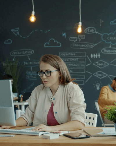 Speciāliste birojā strādā pie datora, pārskatot digitālu saturu un tekstus. Attēls ilustrē mākslīgā intelekta ietekmi uz tekstu, teksta rediģēšanu un satura kvalitātes pārbaudi.